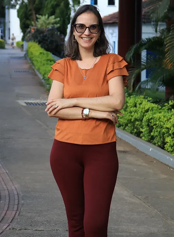 Egressa posa em pé, de camisa laranja, no Campus Coração Eucarístico